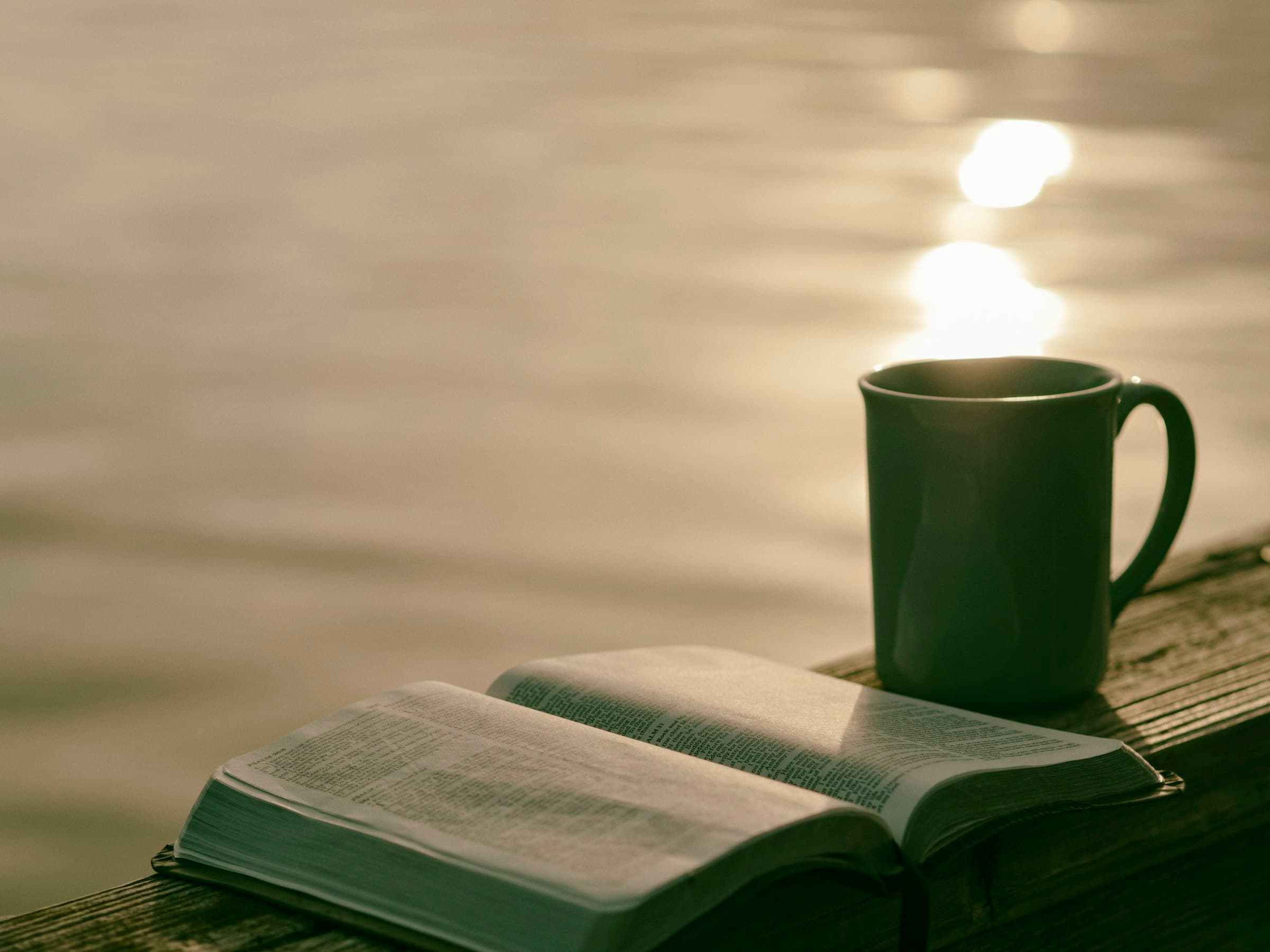 An open Bible beside a mug of coffee in soft morning light